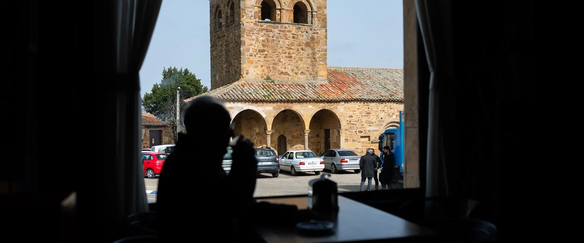 Un hombre toma café. Al fondo, la iglesia y los coches aparcados, en Tábara. Foto Emilio Fraile